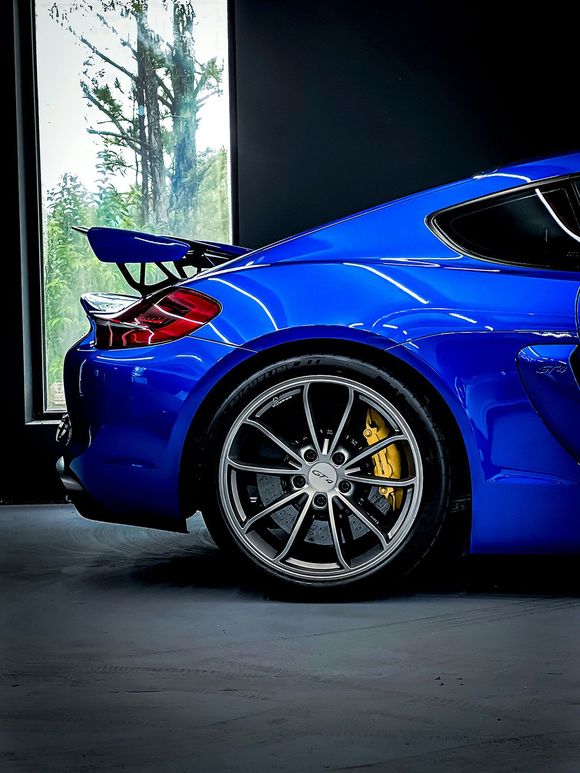 Blue sports car parked indoors with a window in the background. Features a spoiler, alloy wheels and yellow brake calipers.