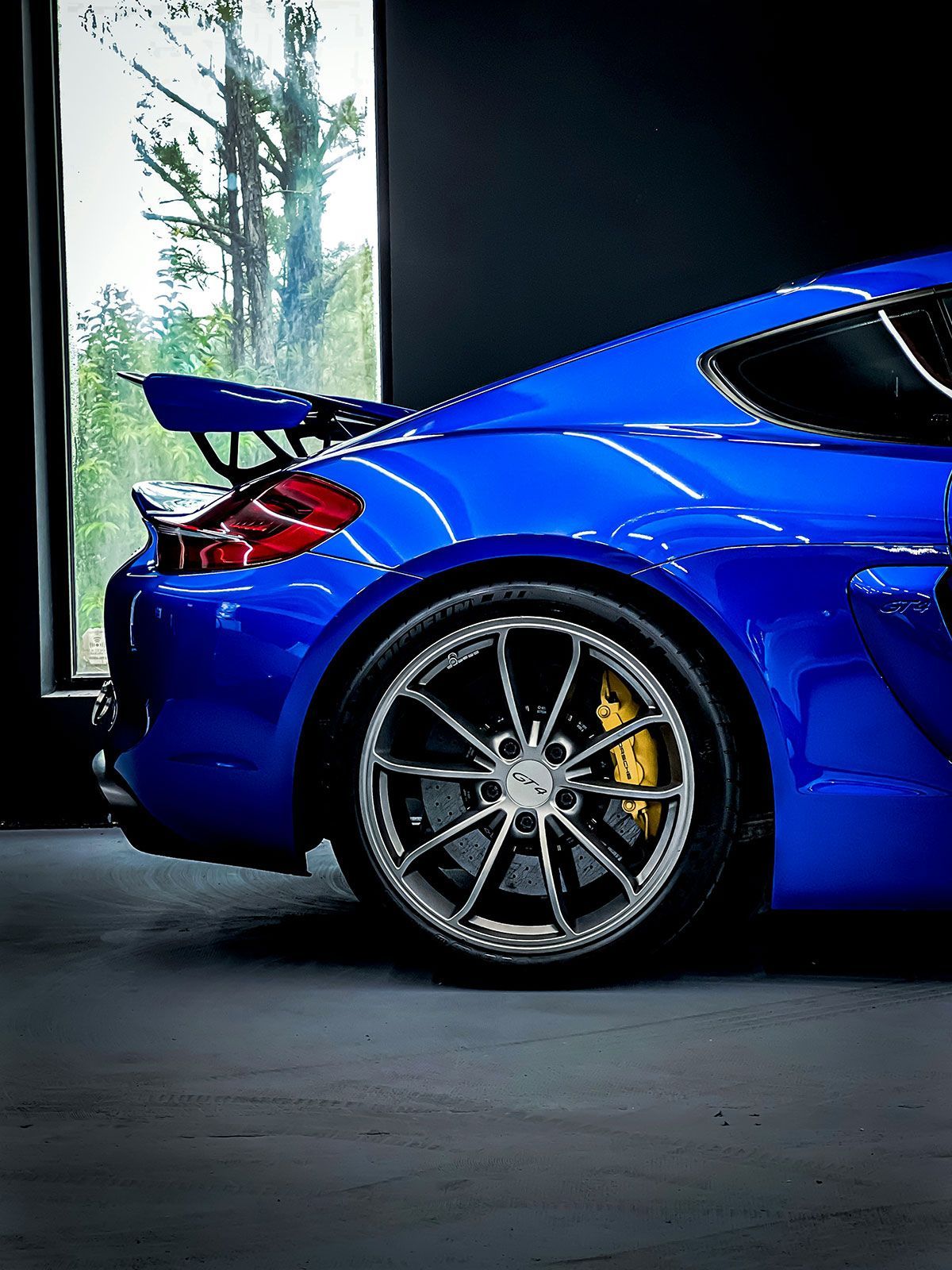 Blue sports car with a spoiler, parked inside near a window, black background.
