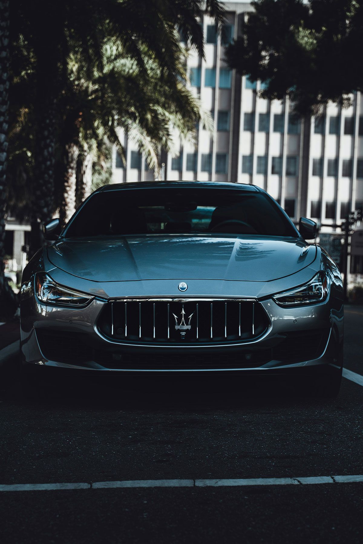 Silver Maserati sedan parked in front of a tall building.