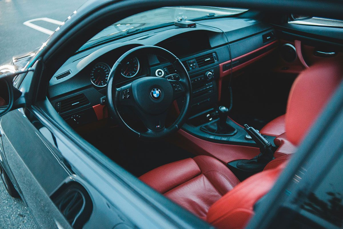 Black BMW car interior with red leather seats and accents. Steering wheel and dashboard visible.